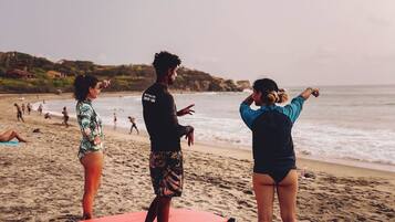 Tres personas de pie en una playa con tablas de surf, cielo despejado y mar tranquilo.