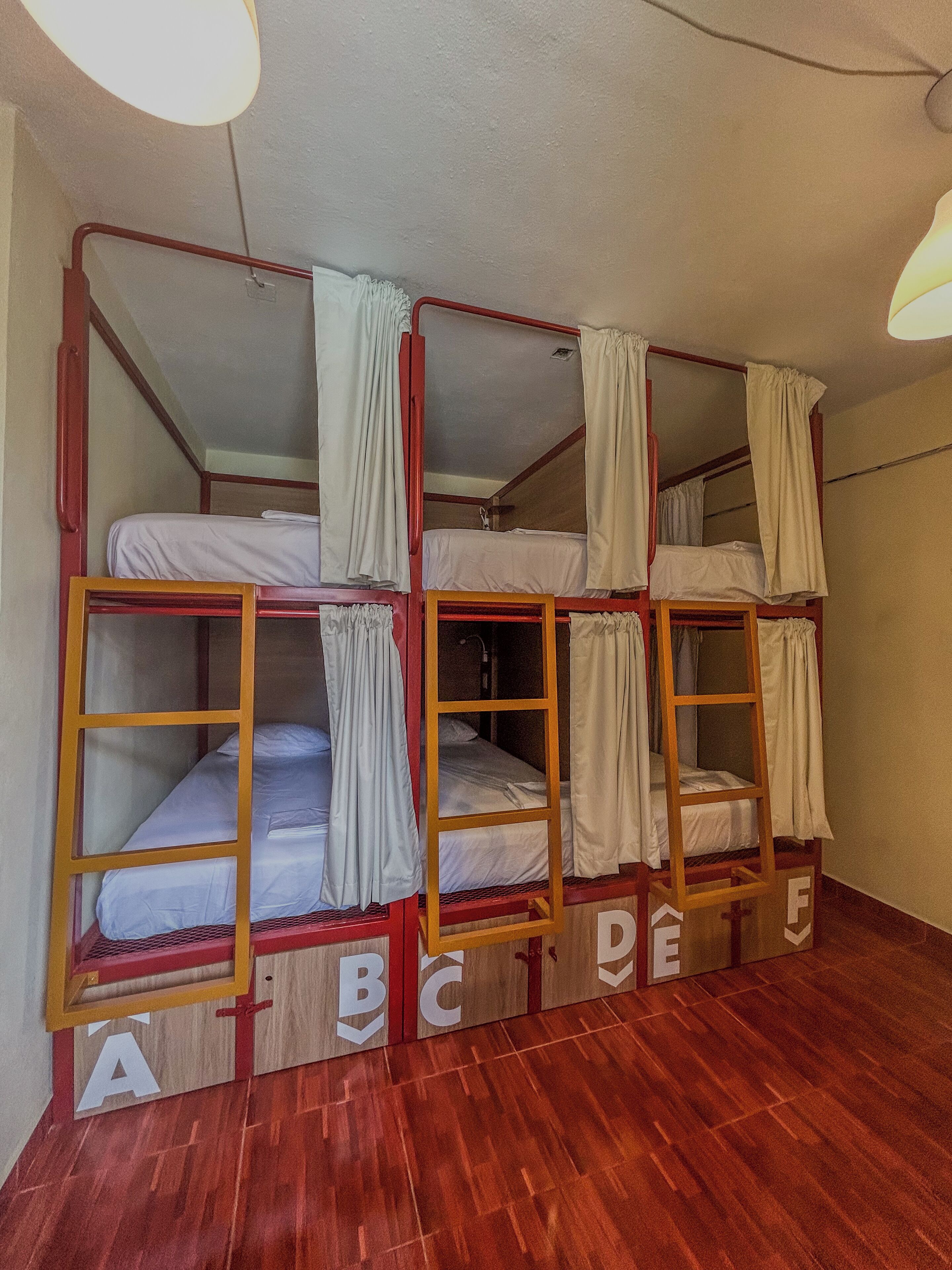 Ein Schlafsaalzimmer mit Stockbetten, Holzrahmen und Vorhängen.