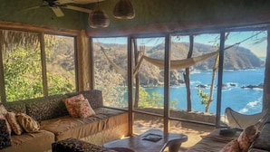 Une pièce chaleureuse avec de grandes fenêtres donnant sur un paysage côtier magnifique, comprenant un canapé et une table basse.