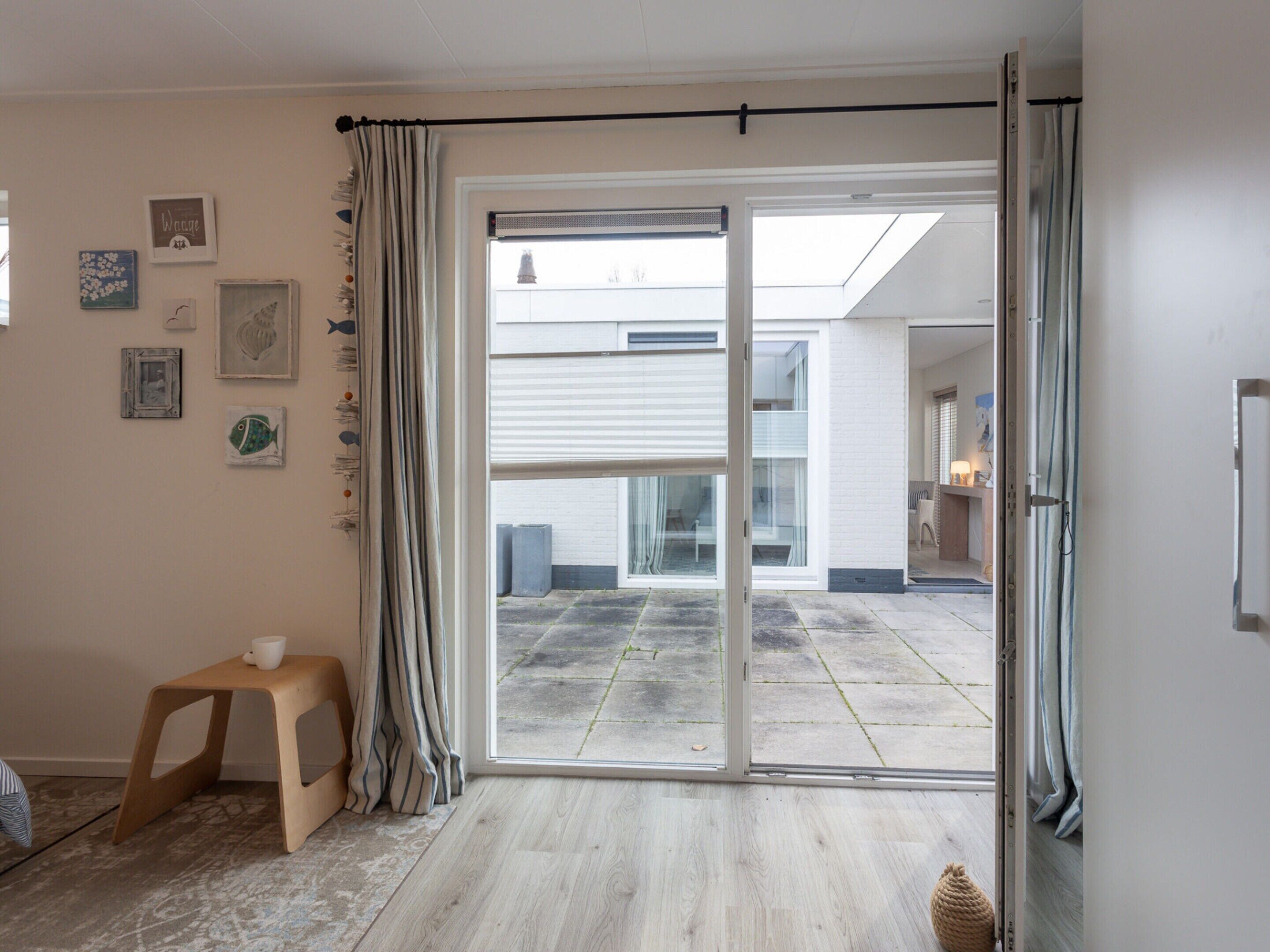 A room with a sliding glass door leading to a balcony, a small stool, and various wall decorations.