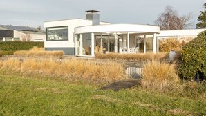 A modern house with a glass conservatory, a chimney, and a garden with dry grass. - Holiday Home by Lake Veerse Meer (Kamperland)