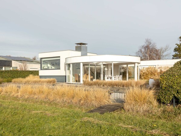 A modern house with a glass conservatory, a chimney, and a garden with dry grass.