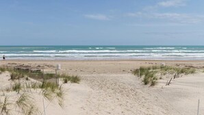 Ein sandiger Strand mit Wellen, einem Zaun und etwas Vegetation.