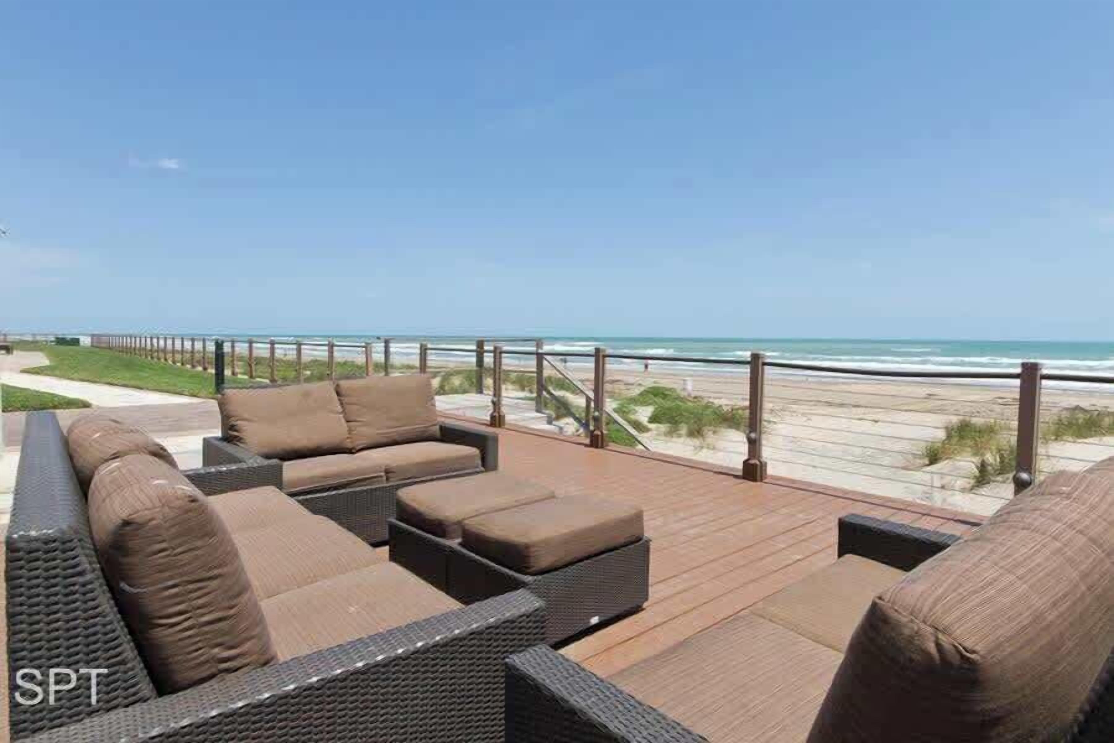 A deck with wicker furniture and a view of the beach.