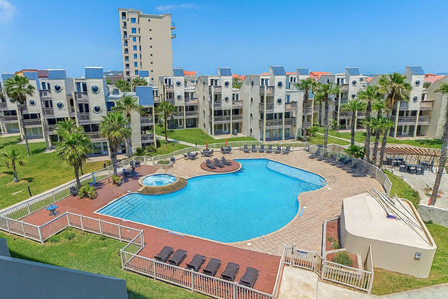 A hotel with a swimming pool, palm trees, and a view of other buildings.