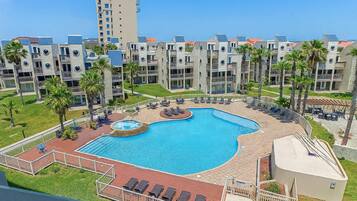 A hotel with a swimming pool, palm trees, and a view of other buildings.