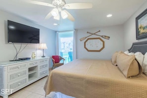 Une chambre à coucher avec un lit, une télévision, un ventilateur de plafond, une commode et une fenêtre.