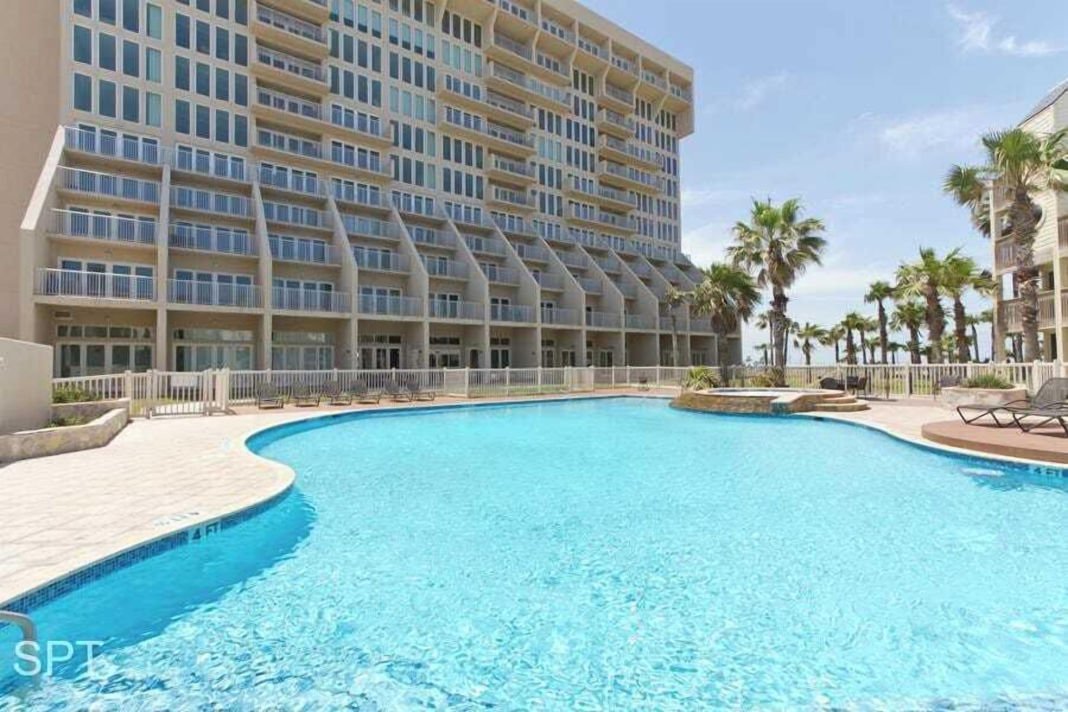 A hotel with a large pool, multiple balconies, and palm trees.