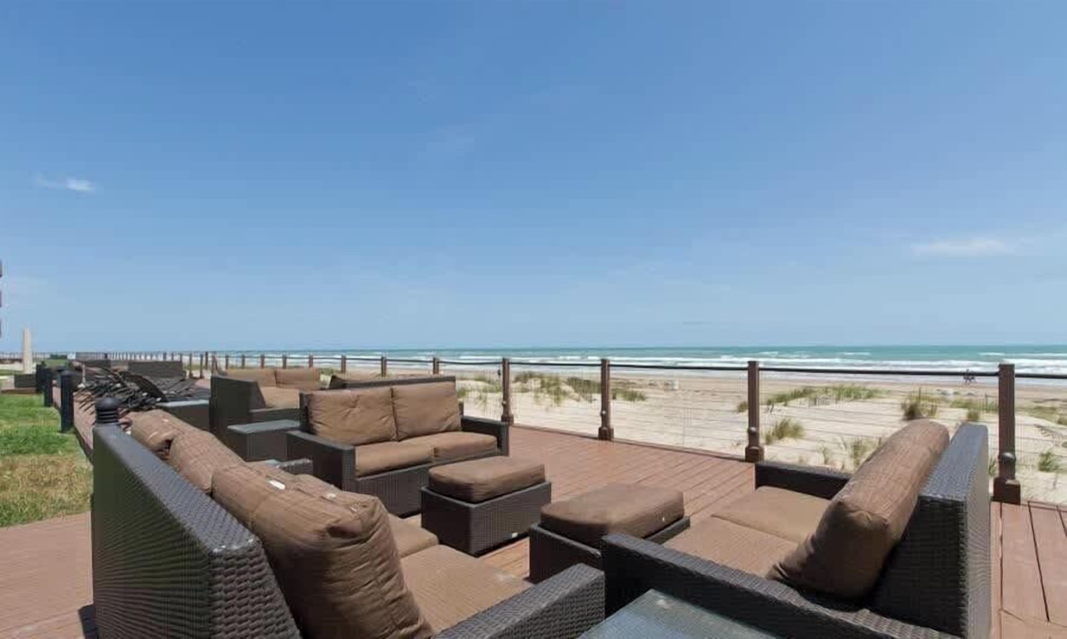 A deck with wicker furniture and a view of the beach.