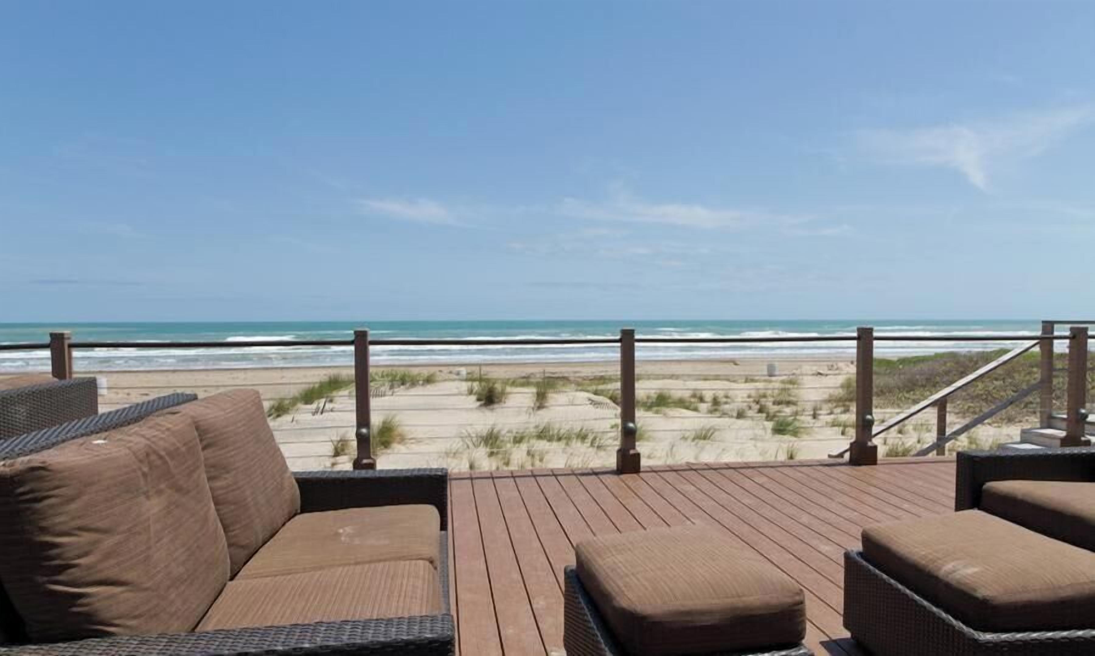 Een houten terras met rieten meubilair met uitzicht op een strand.