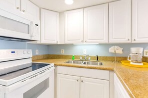 A kitchen with white cabinets, a stainless steel sink, a coffee maker, and a microwave.