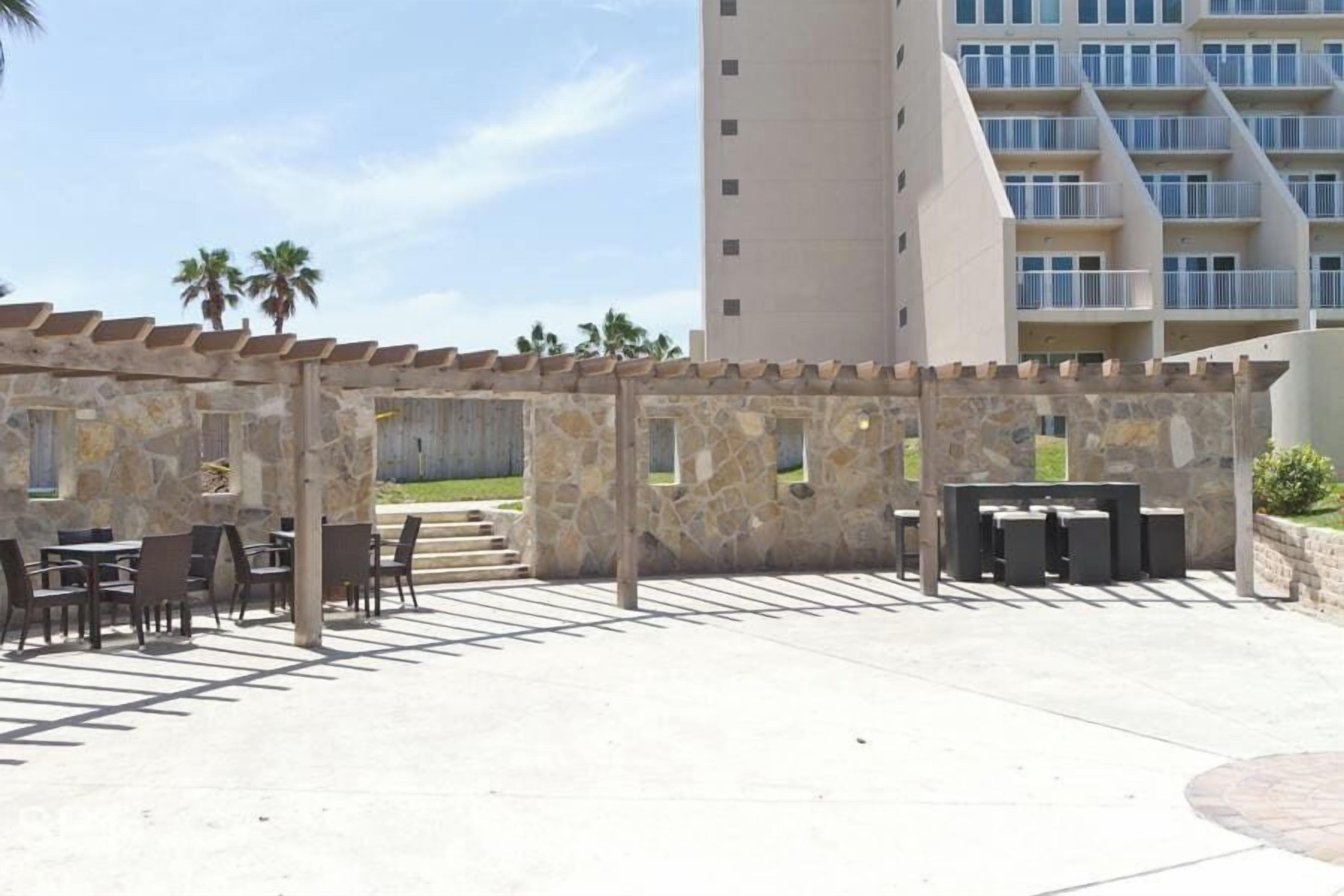 An outdoor patio area with stone walls and tables, overlooking a modern building with balconies.