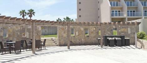 An outdoor patio area with stone walls and tables, overlooking a modern building with balconies.