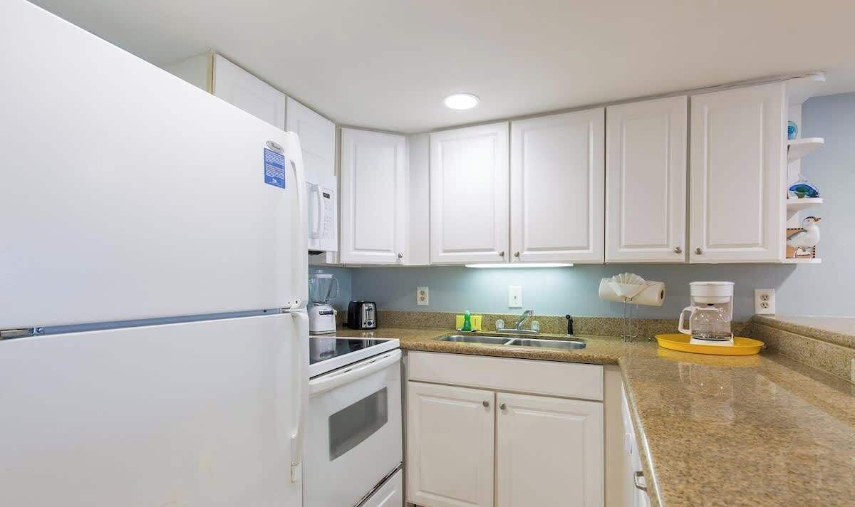 A kitchen with white cabinets, a refrigerator, a stove, a coffee maker, and a sink.