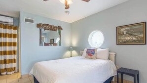 Een slaapkamer met een bed, een plafondventilator, een raam, een schilderij en een bord aan de muur.
