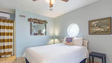 A bedroom with a bed, a ceiling fan, a window, a painting, and a sign on the wall.