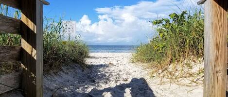 A sandy beach path leading to the ocean with wooden structures on either side.