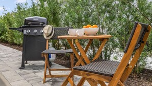 An outdoor patio with a grill, wicker chairs, a small table, and a bowl of oranges. - Seas the Day Beach Wine Dine Relax (Naples)