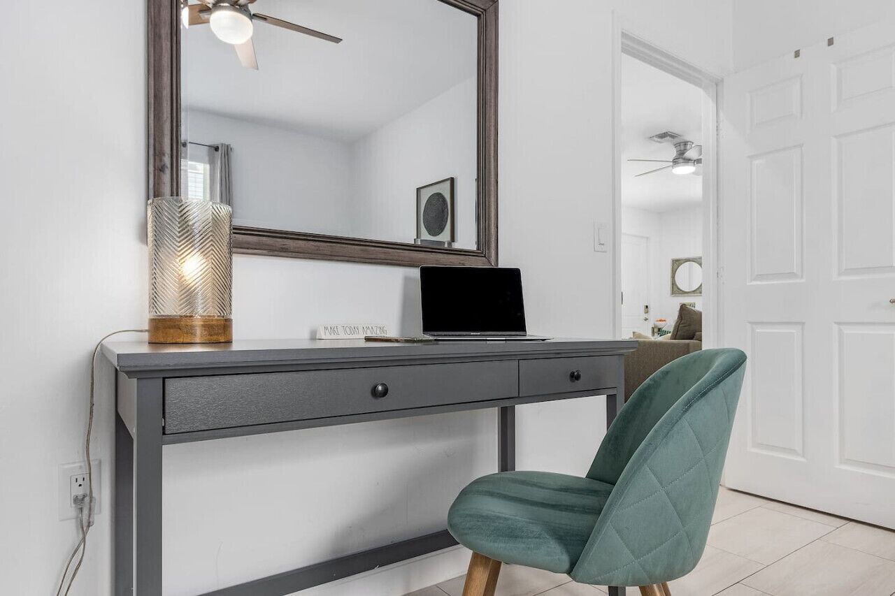 A modern room with a desk, a laptop, a green chair, a large mirror, and a decorative lamp.