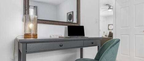 A modern room with a desk, a laptop, a green chair, a large mirror, and a decorative lamp.
