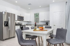 Una cocina moderna con gabinetes blancos, electrodomésticos de acero inoxidable y una mesa de comedor con sillas.