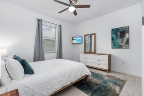 A bedroom with a bed, a ceiling fan, a television, a dresser, and a painting on the wall.