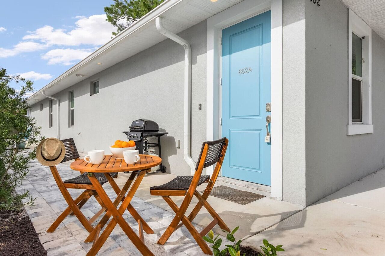 A patio with a table and chairs, a blue door, and a barbecue grill.