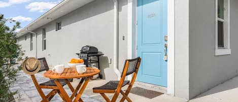 Un patio con mesa y sillas, una puerta azul y una parrilla.