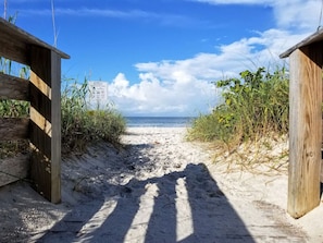 A sandy beach path leading to the ocean with wooden structures on either side.