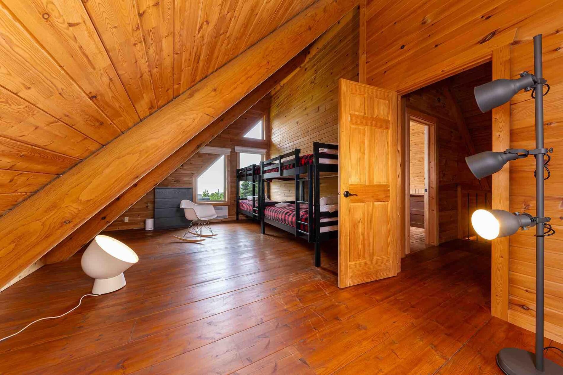 Une chambre mansardée en bois avec des lits superposés, un fauteuil à bascule et un bureau.