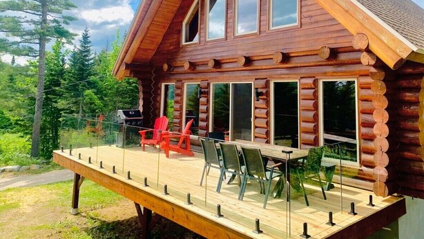 Een houten chalet met een terras, grote ramen en buitenmeubels.