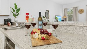 A kitchen with a marble countertop, a wooden cutting board with cheese and grapes, and wine glasses. - Paradise at Hidden Palms Cove (Fort Myers)