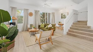 A spacious living room with a green sofa, wooden coffee table, and a large plant. A staircase with carpeted steps leads to another level. - Paradise at Hidden Palms Cove (Fort Myers)