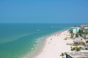 A beach with clear turquoise waters, a pier extending into the sea, and buildings with balconies overlooking the beach. - Beach, pool time & fun times @ Blue Fish Lagoon (Fort Myers Beach)
