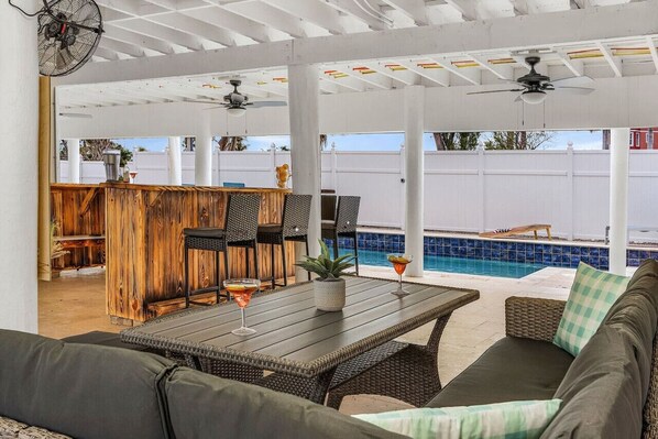 An outdoor patio with a pool, seating area, and a bar.