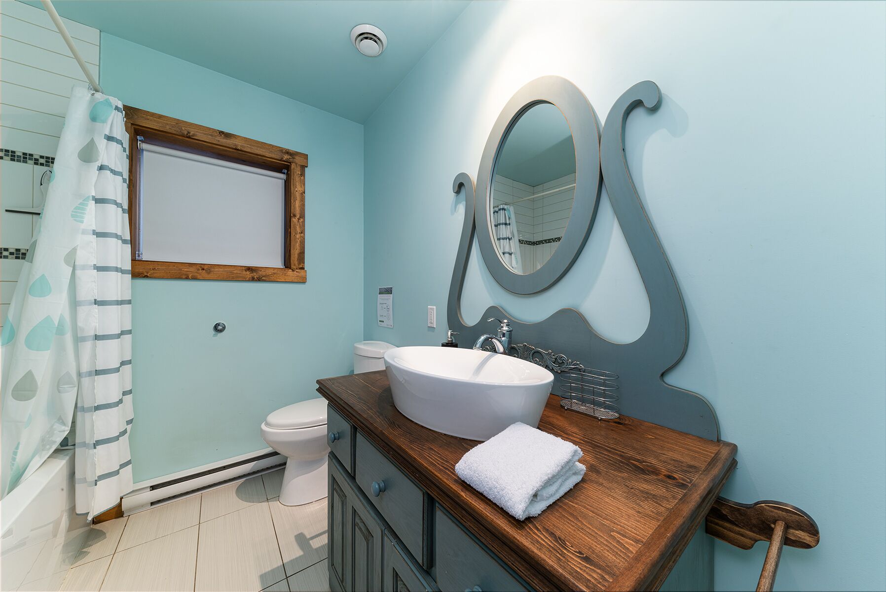 Une salle de bain avec un meuble-lavabo en bois, un lavabo blanc, un miroir et un rideau de douche.