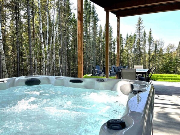 A hot tub with a wooden deck and chairs, surrounded by a forest.
