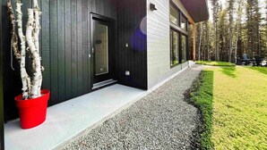 Une maison moderne à l’extérieur sombre, dotée d’une porte en verre et d’un chemin de gravier menant à une zone herbeuse.