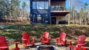 Una casa moderna de dos pisos con ventanas grandes y una terraza, rodeada de un bosque.