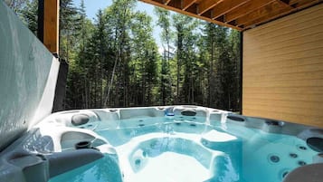 Un bain à remous doté de plusieurs jets, entouré d’une terrasse en bois et avec une forêt en arrière-plan.