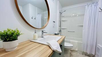 Une salle de bain moderne avec un meuble-lavabo en bois, un miroir rond, un lavabo, des toilettes et un espace douche.