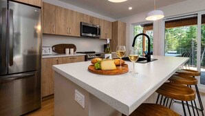 Una cocina moderna con una isla central, electrodomésticos de acero inoxidable, armarios de madera y un amplio ventanal con vistas al verdor.