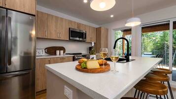 A modern kitchen with a central island, stainless steel appliances, wooden cabinets, and a large window providing a view of greenery.