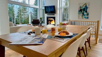 Un coin repas avec une table en bois, des chaises blanches, des aliments pour le petit-déjeuner et une cheminée.