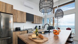 Une cuisine moderne dotée d’un grand îlot central, de meubles en bois, d’appareils électroménagers en acier inoxydable et offrant une vue sur l’eau.