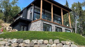 Une maison moderne à deux étages, avec des fondations en pierre, de grandes fenêtres et un balcon en bois.