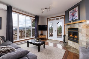 Uma sala de estar ampla com lareira, uma televisão grande e uma vista panorâmica pelas portas de vidro.