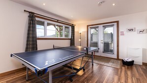 A ping pong table in a room with wooden flooring, large windows, and a door with blinds. - Condo 120B: Hot Tub, Panoramic Views & Game Area (Charlevoix)
