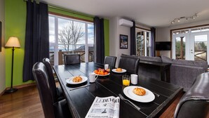 A dining area with a table set for breakfast, a sofa, and a view of the outdoors. - Condo 120B: Hot Tub, Panoramic Views & Game Area (Charlevoix)