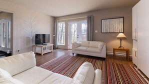 A modern living room with a sofa, a television, a lamp, and a patterned rug. - Le Méridien 33: Spa, River Views, Near Le Massif (Petite-Rivière-Saint-François)